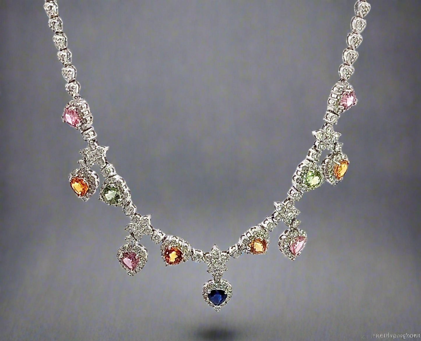 hanging white gold diamond necklace with 4 pink heart-shaped stones, 4 orange heart shaped stones, 2 green heart shaped stones, and 1 centered blue heart shape stone