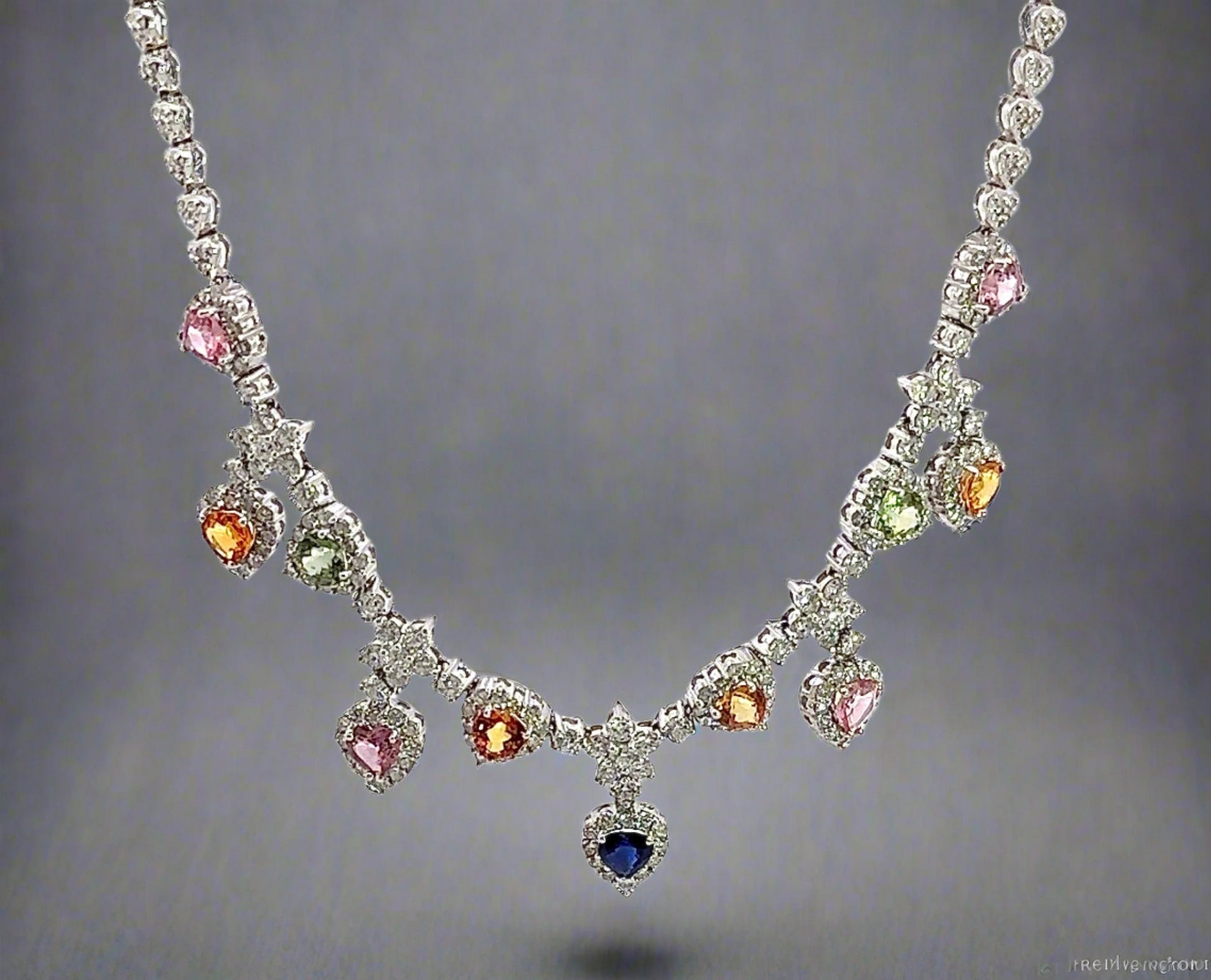 hanging white gold diamond necklace with 4 pink heart-shaped stones, 4 orange heart shaped stones, 2 green heart shaped stones, and 1 centered blue heart shape stone