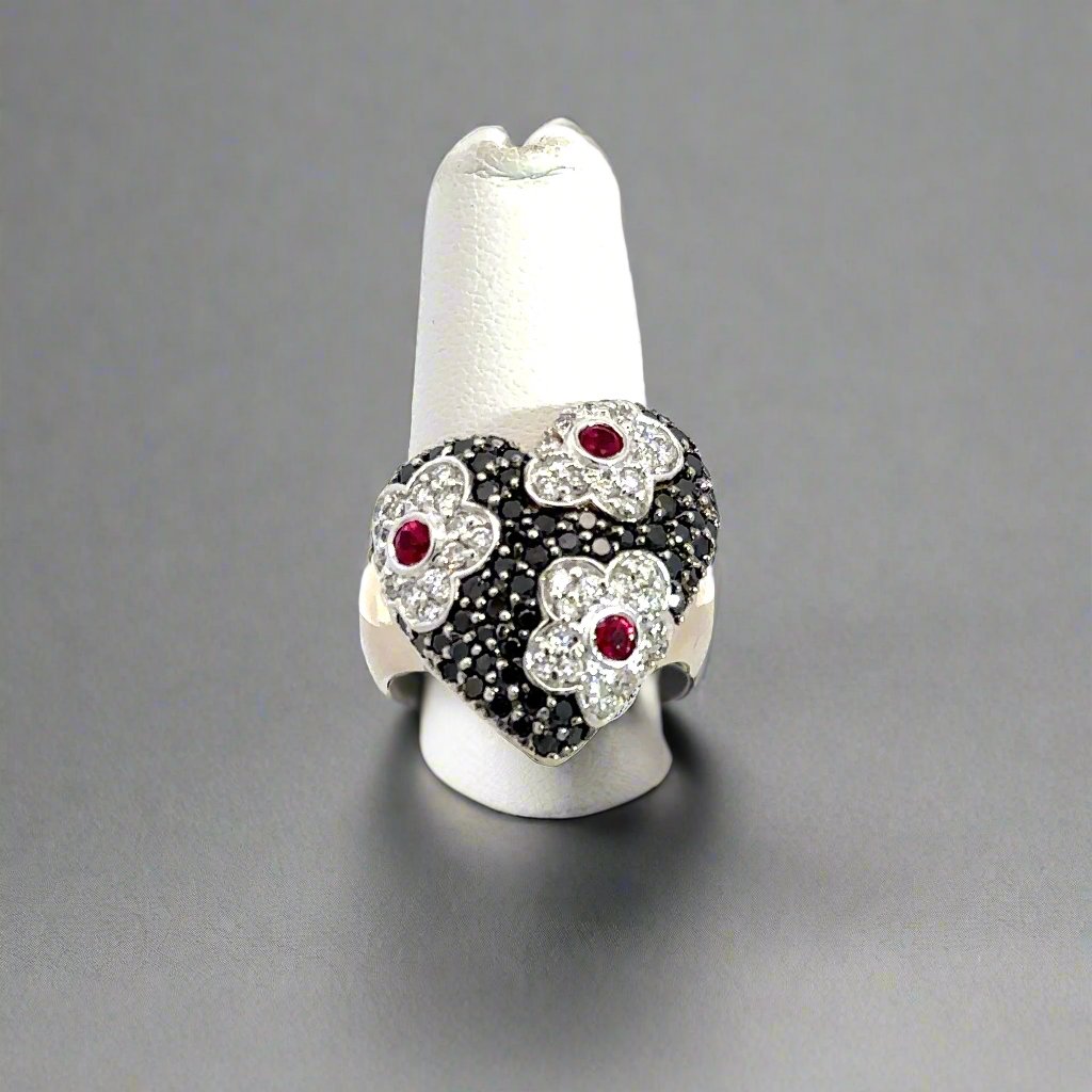 front of heart ring with flower detailing and black and white small round diamonds and 3 ruby gemstones