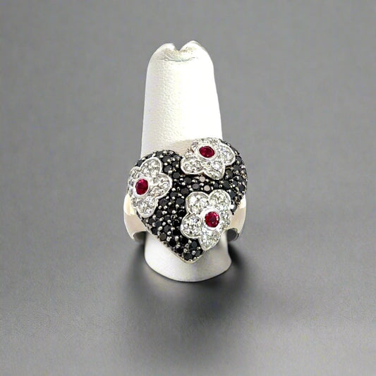 front of heart ring with flower detailing and black and white small round diamonds and 3 ruby gemstones