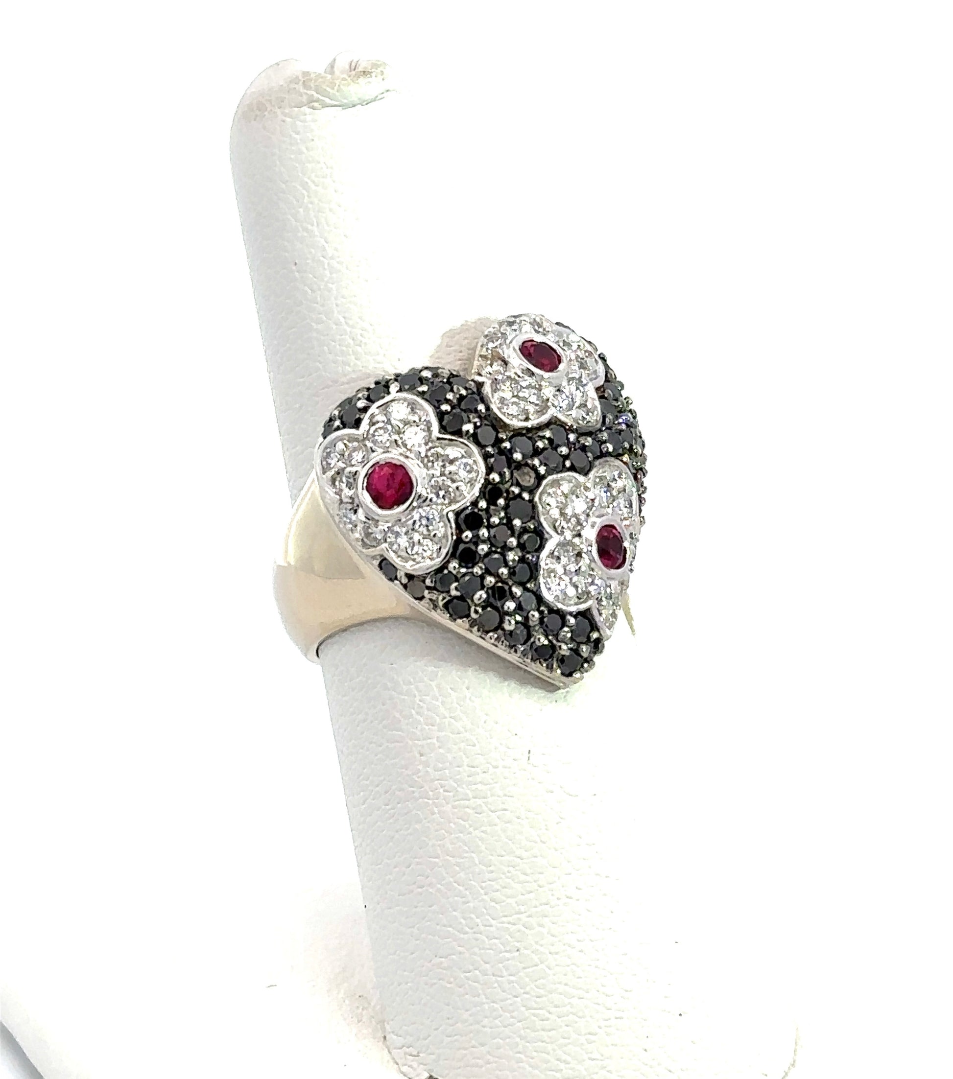 Diagonal view of heart-shaped diamond ring with black and white diamonds and 3 rubies.