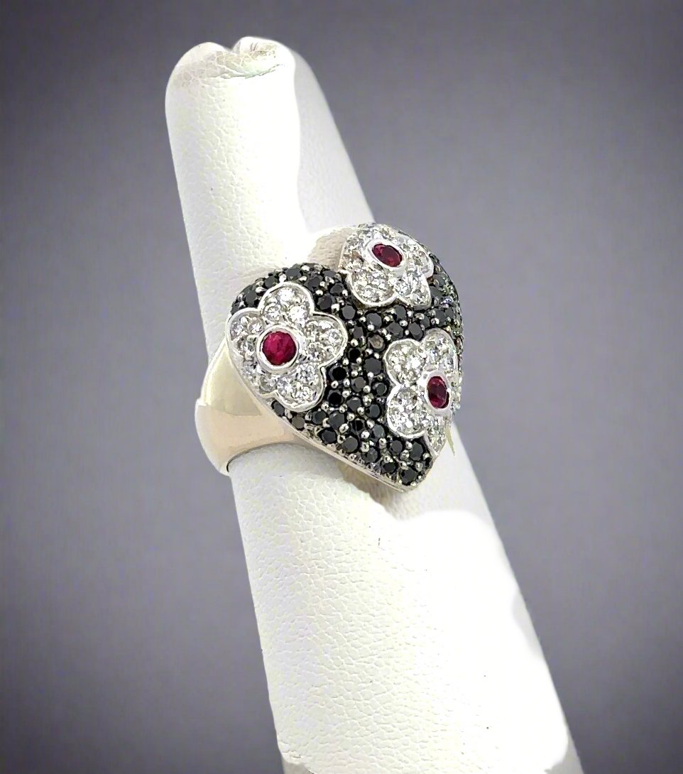 Diagonal view of heart-shaped diamond ring with black and white diamonds and 3 rubies.