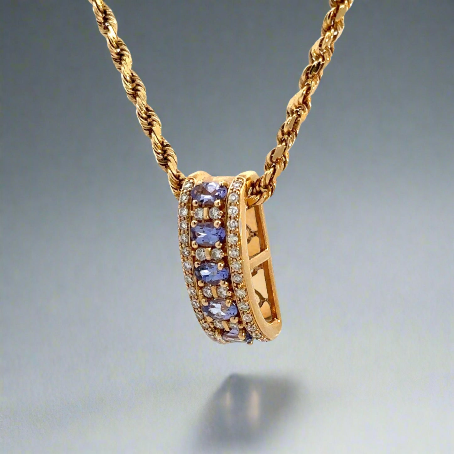Diagonal view of yellow gold rope chain and yellow gold pendant with diamonds and tanzanite gemstones