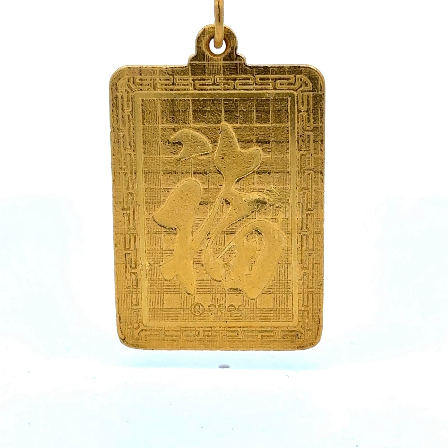 close up of back of the pendant with a chinese symbol, scratches, and a small dent on the gold