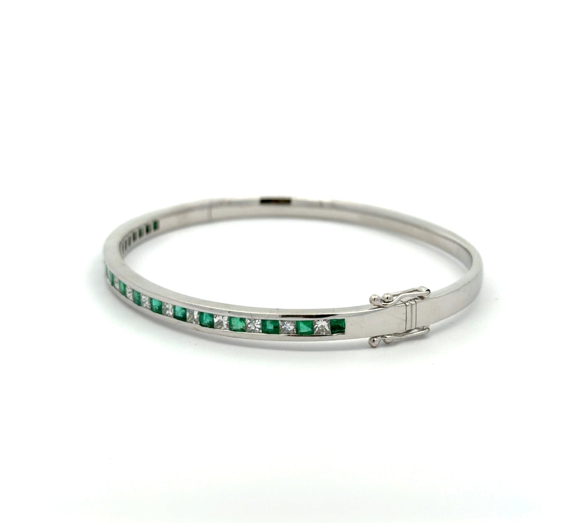 Diagonal view of white gold princess-cut diamond and emerald bangle bracelet on white background