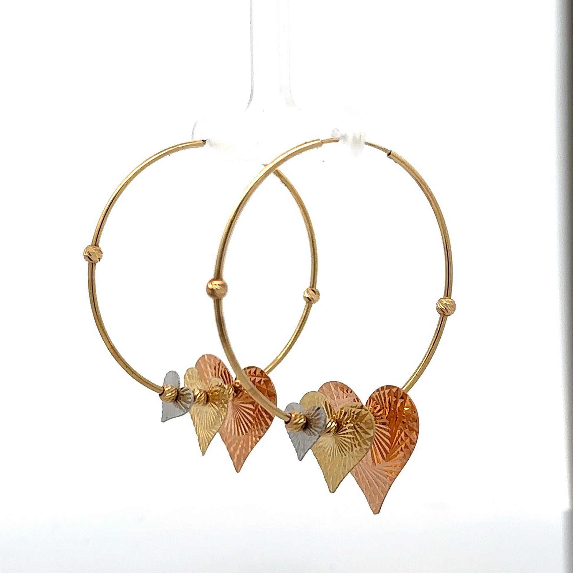 Diagonal view of yellow gold hoops with rose, white, and yellow gold hearts