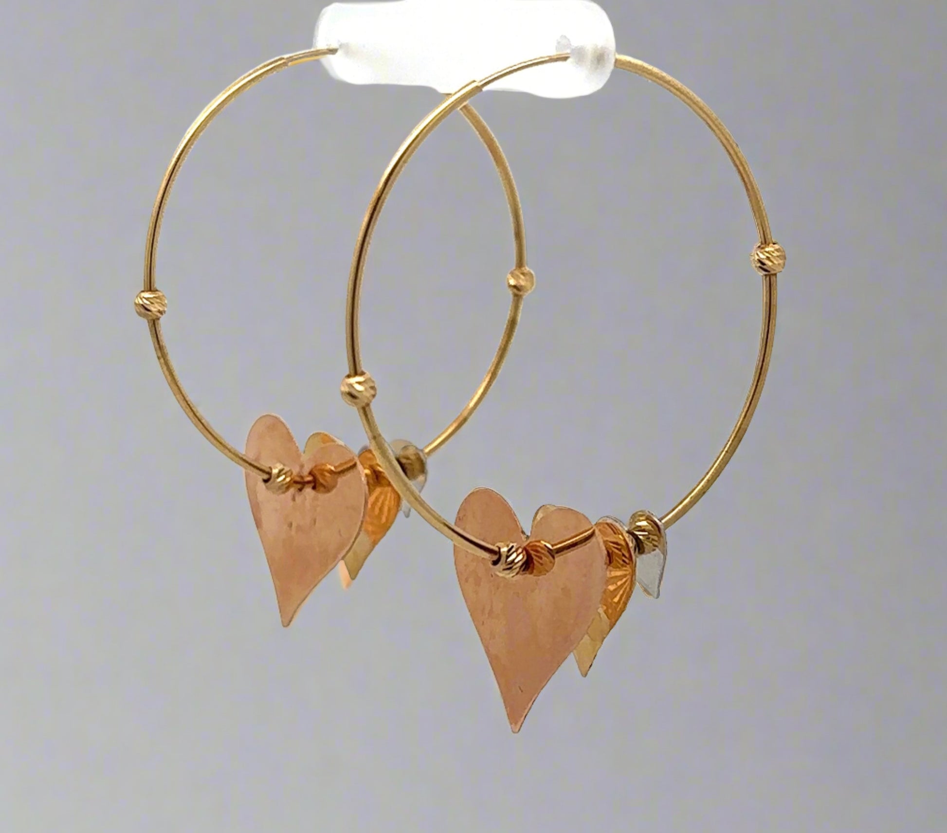 Diagonal view of yellow gold hoops with hanging hearts
