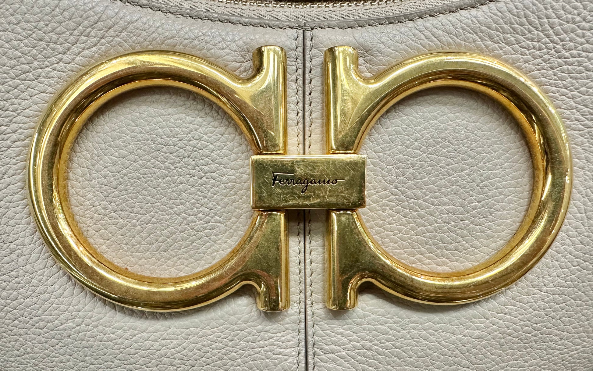 Close up photo of Ferragamo logo on front in gold with scratches on hardware