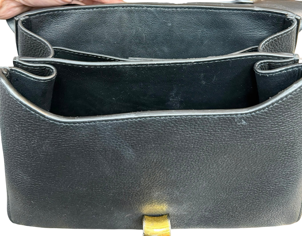 Close-up of the interior of a black pebbled leather handbag, showing the open compartments and a small gold-tone clasp at the bottom.