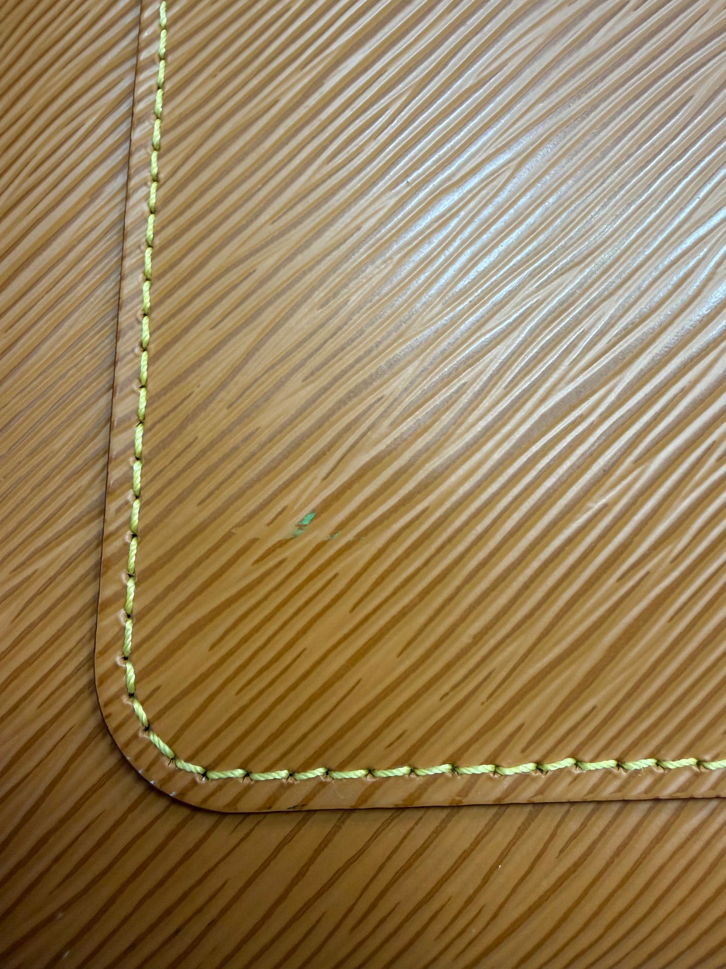 Close-up of a brown textured leather corner with light yellow stitching with a small light green-colored stain