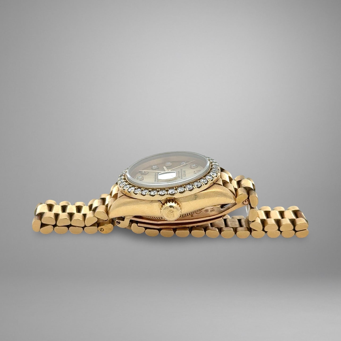 Gold wristwatch with diamond-studded bezel on a gray background