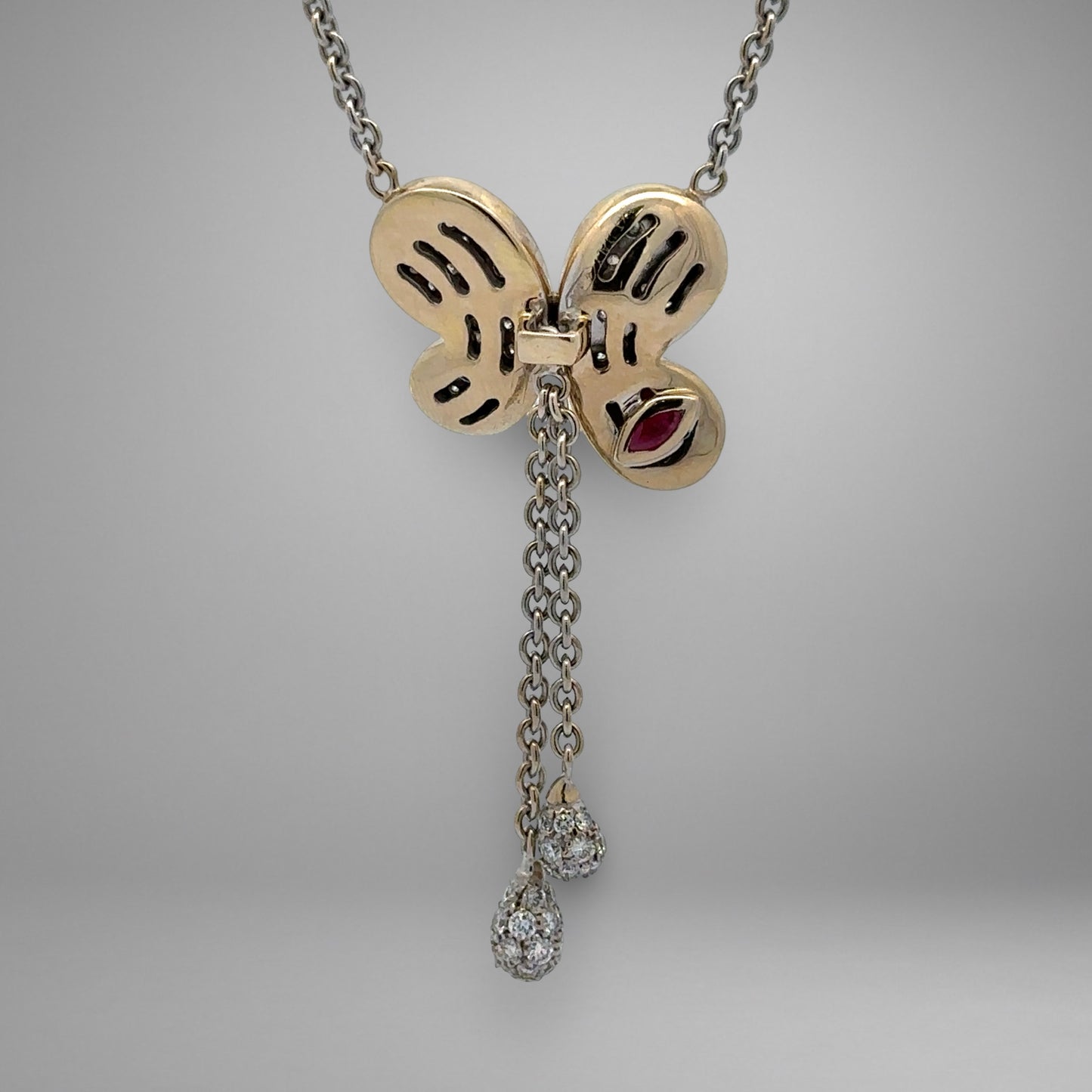 Butterfly-shaped pendant with chain and gemstones on a gray background
