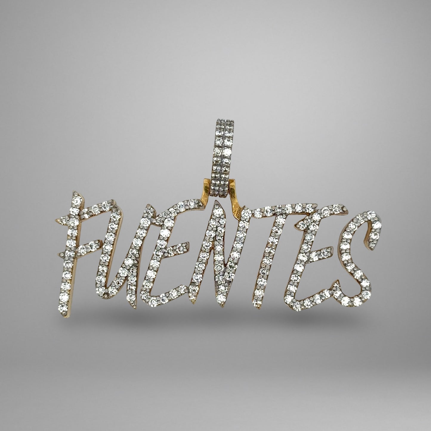 Diamond-studded pendant with the word 'FUENTES on a gray background