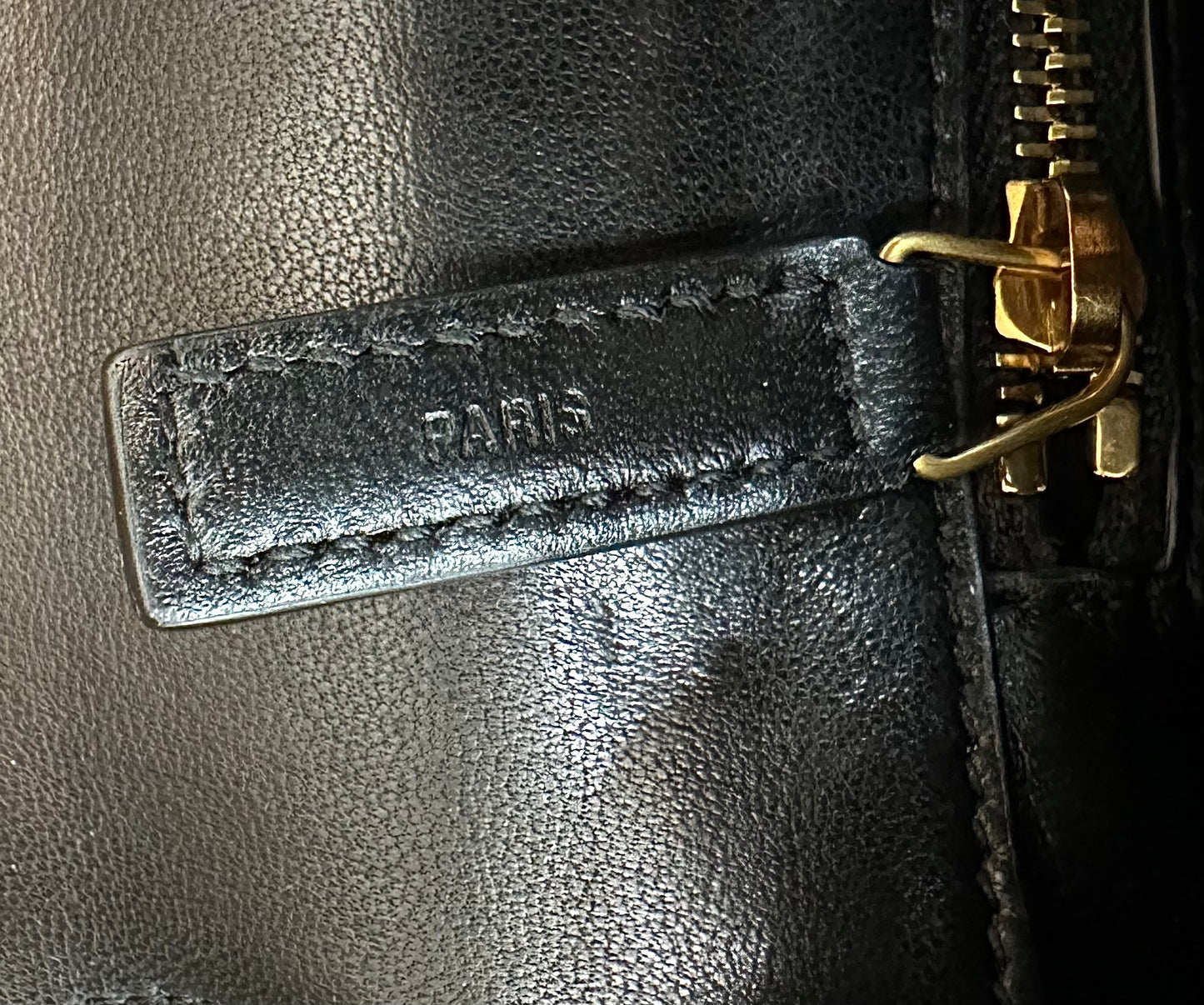 Close up of zipper with Paris embossed in black leather and gold hardware