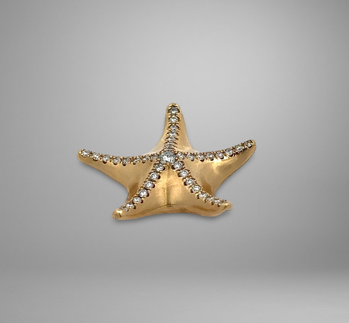Gold starfish-shaped jewelry with embedded stones on a gray background