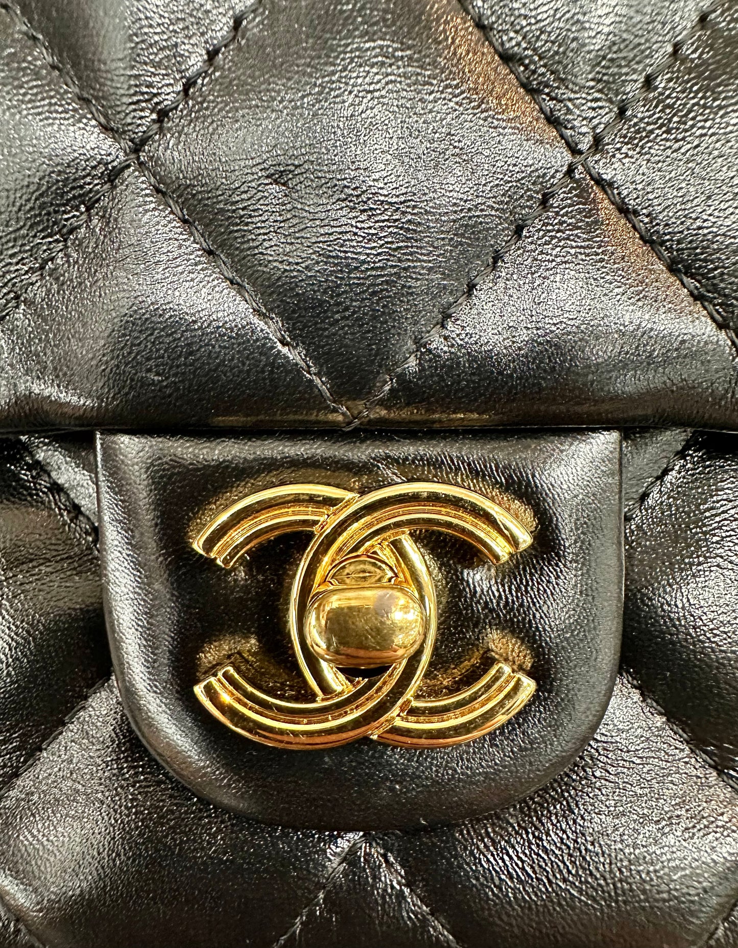 Close up of Chanel gold hardware logo with lock on front exterior of bag with scratches on the hardware