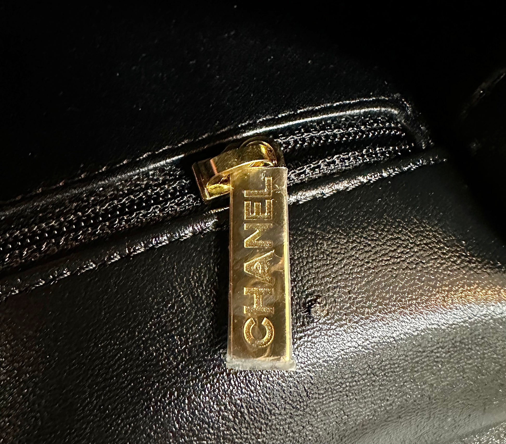 Close up of Chanel engraved on gold interior zipper with plastic still on it.