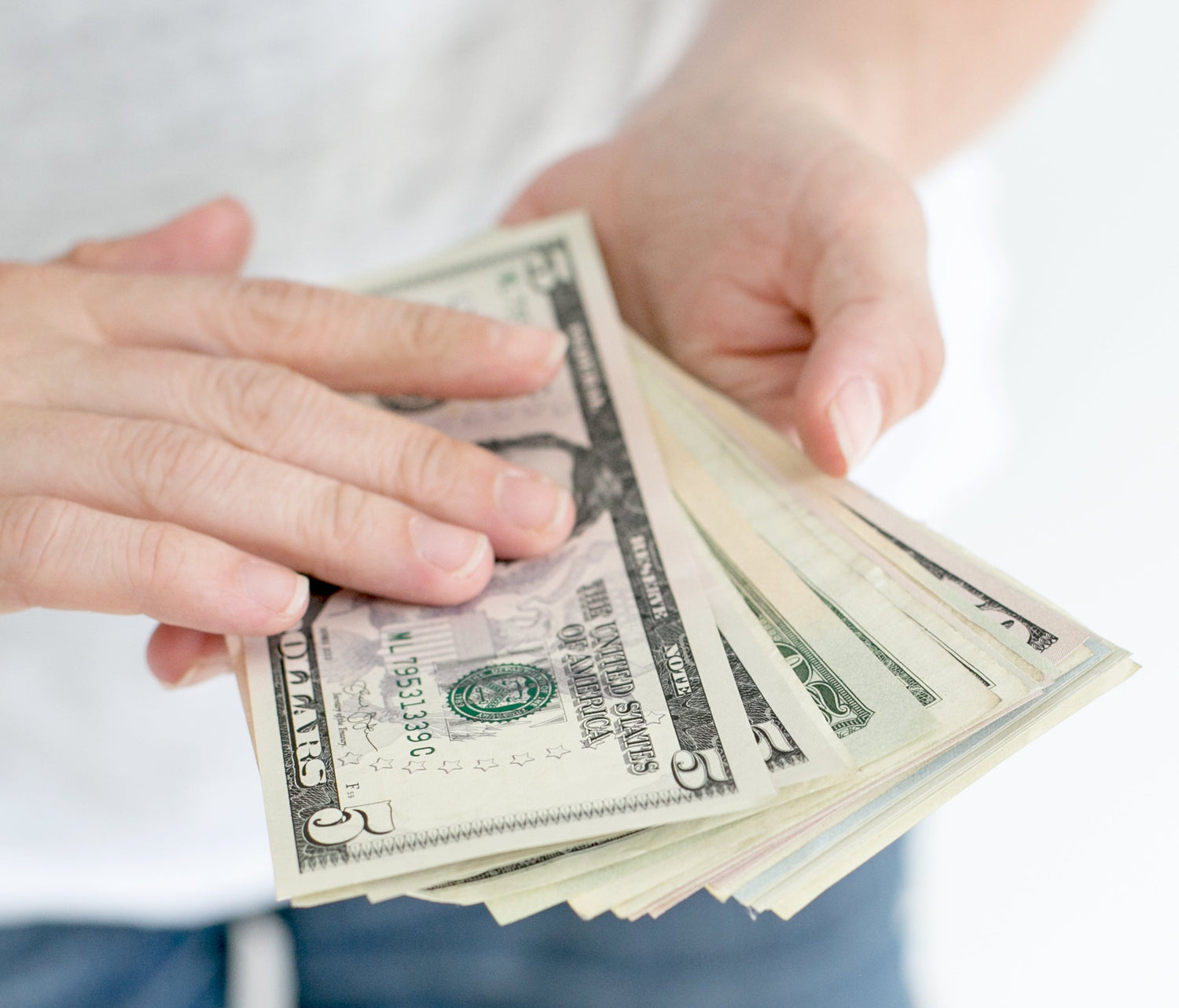 Two hands holding a stack of U.S. dollar bills.