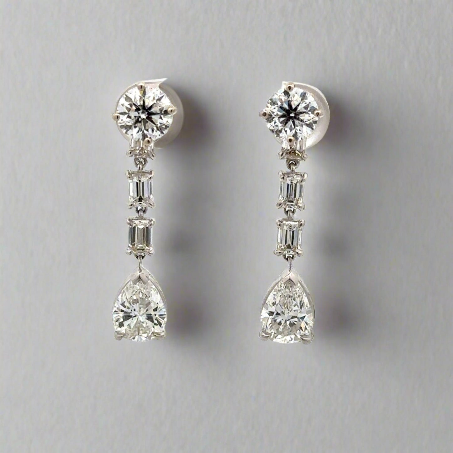 Diamond drop earrings with 1 carat round diamond at top, 2 .20 carat emerald cut diamonds below, + 1 .75 carat pear shaped diamonds at bottom