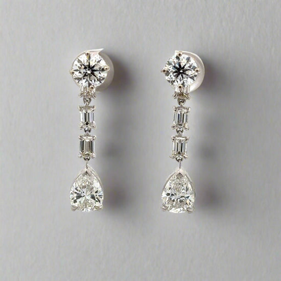 Diamond drop earrings with 1 carat round diamond at top, 2 .20 carat emerald cut diamonds below, + 1 .75 carat pear shaped diamonds at bottom