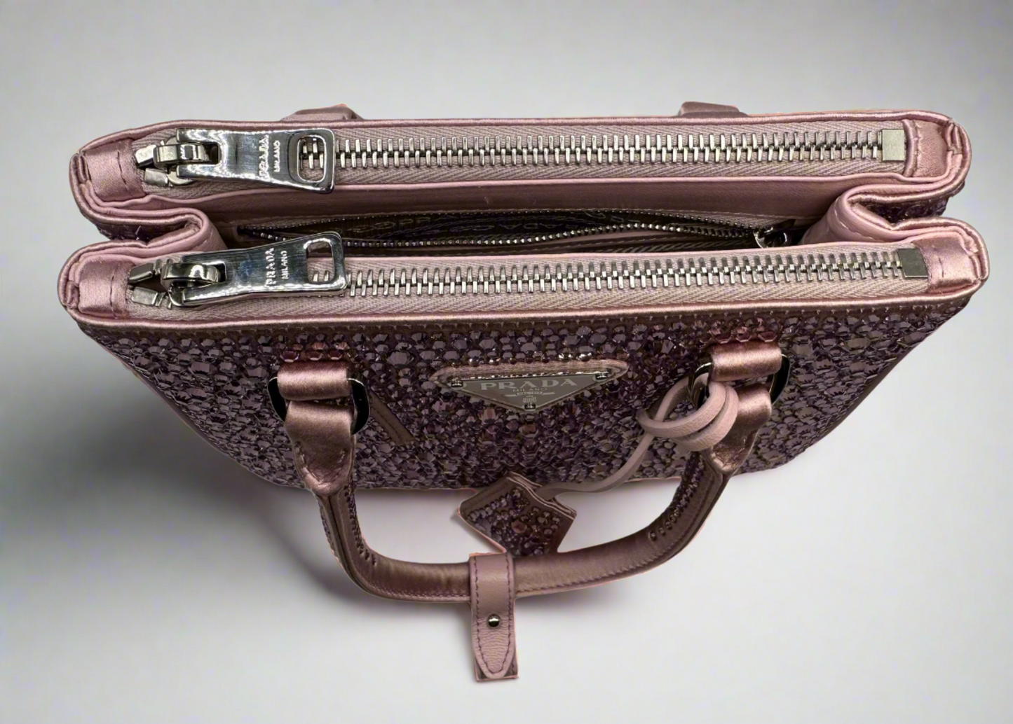 Pictured: The top of the Prada Galleria Crystal mini satin bag in pink with the buttons and zippers closed to show how the bag would look closed. No imperfections.