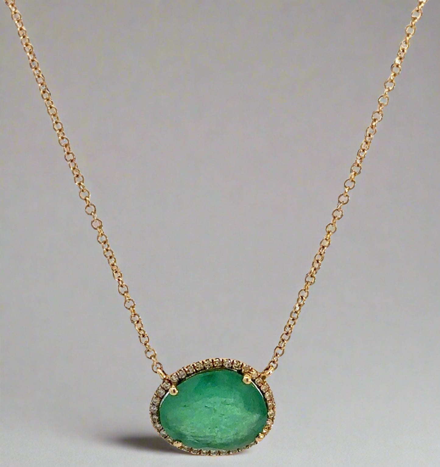 Hanging yellow gold necklace with a free-form emerald and small round diamonds around it