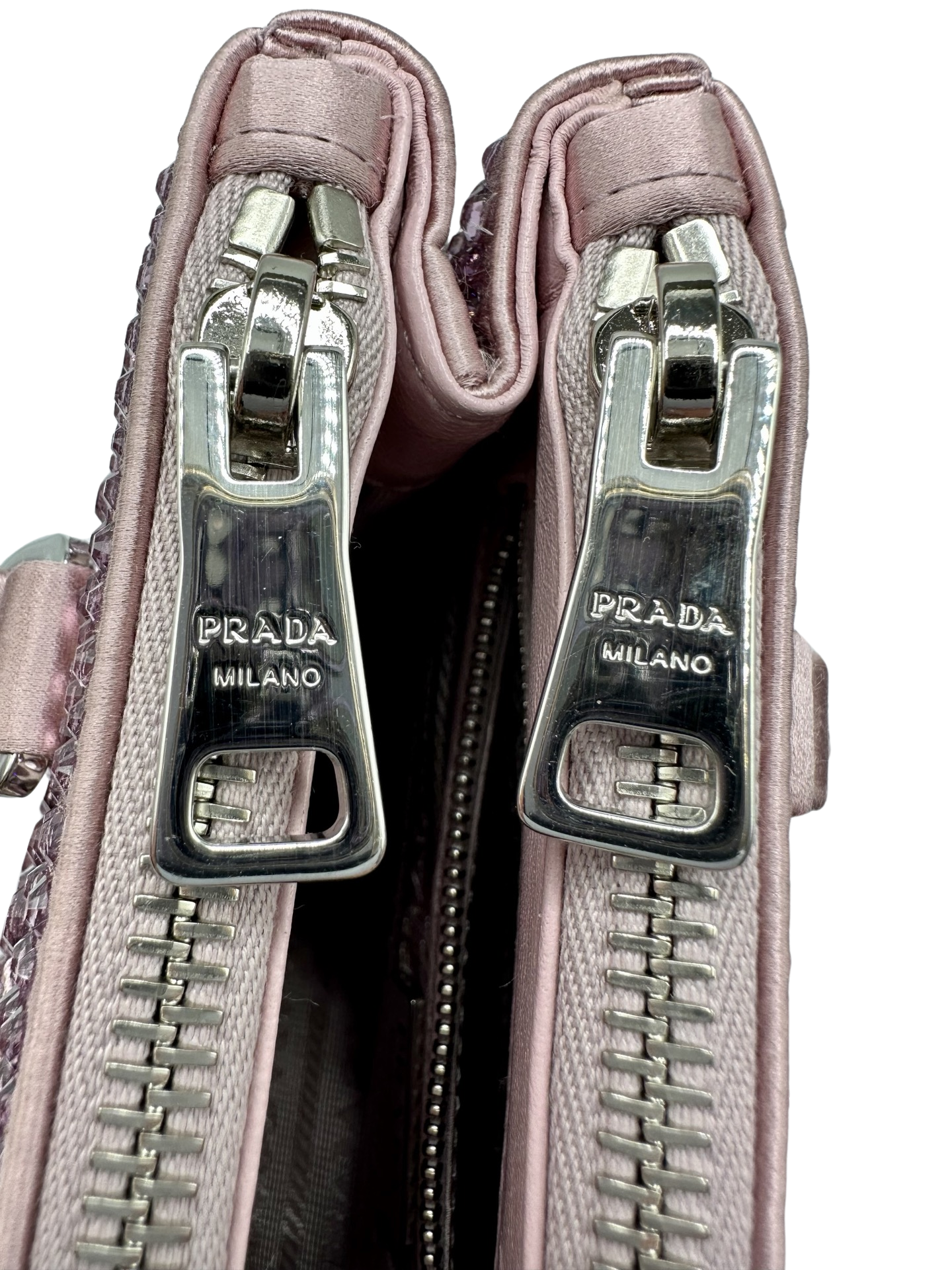 Pictured: Close up of the 2 zippers on the top pockets of the Prada Galleria Crystal mini satin bag in pink. There are very small scratches on the zippers. They say Prada Milano on them.
