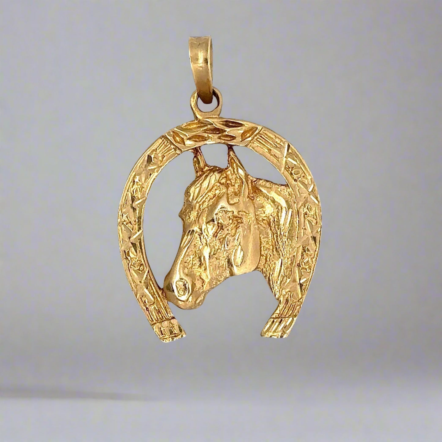 Front of yellow gold horse shoe pendant with a horse head in the middle