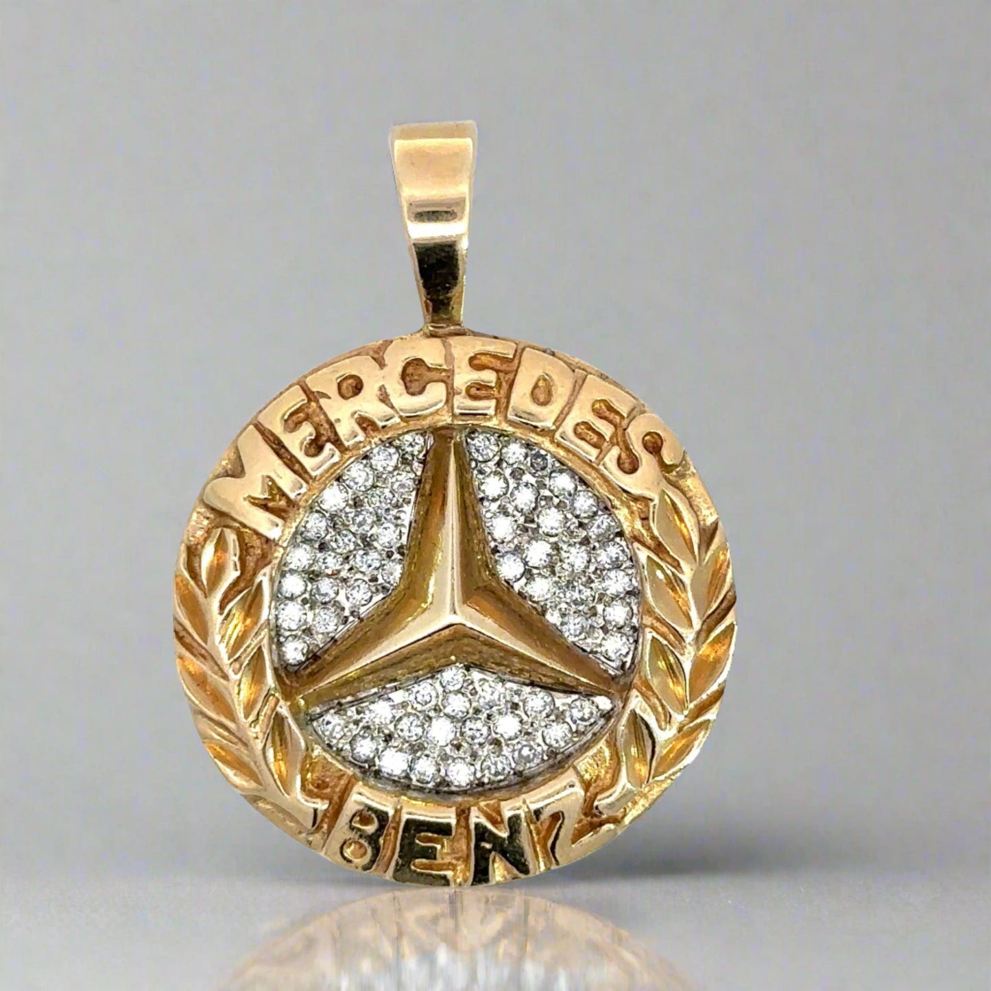 Yellow gold round mercedes benz pendant with mercedes on top and benz on bottom. The logo is in the center with diamonds aroun dit.