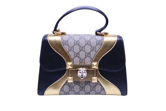 Black and gold gucci bag with black top handle and gg supreme print with white tiger emblem on lock closure in middle