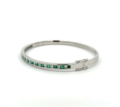 Diagonal view of white gold princess-cut diamond and emerald bangle bracelet on white background