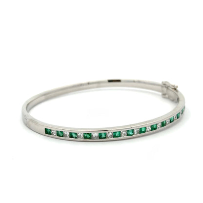Diagonal view of white gold princess-cut diamond and emerald bangle bracelet on white background