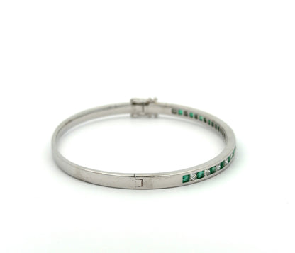 Side of white gold princess-cut diamond and emerald bangle bracelet on white background