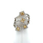 A multi-band ring featuring four square yellow diamonds surrounded by small clear stones, set in a silver-toned metal, displayed on a white cone stand against a white background.