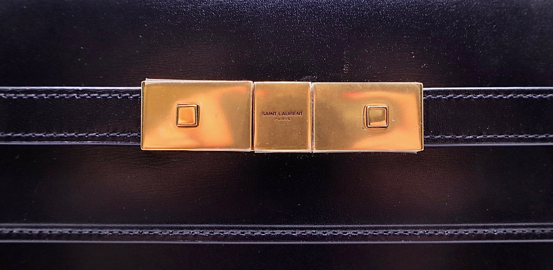 Close up of Saint Laurent gold magentic buckle closure with Saint Laurent logo + protective plastic on it.