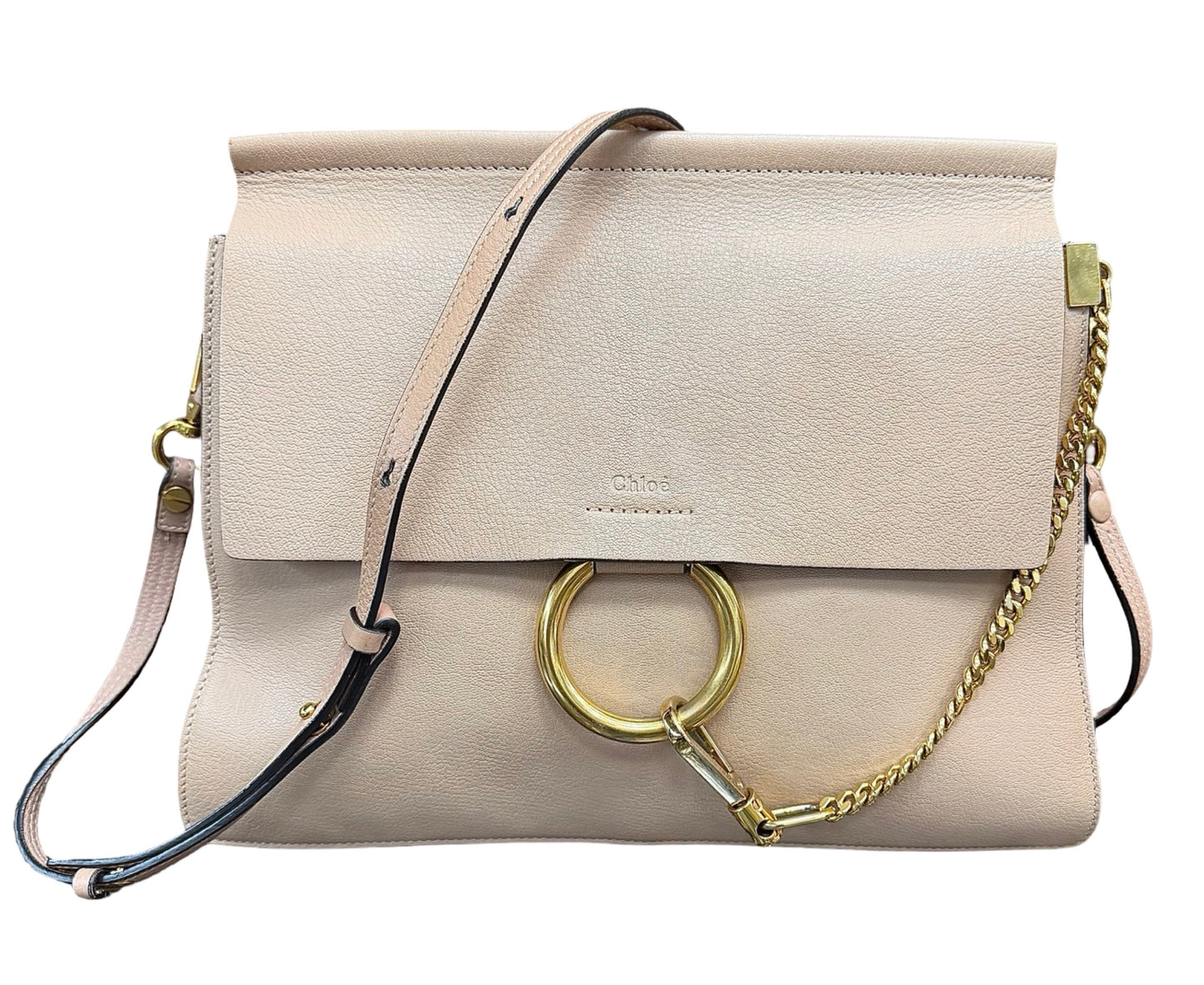 A light beige leather shoulder bag with a flap closure, a large gold-tone O-ring, a gold chain detail, and a thin black-and-beige strap, shown on a plain white background.