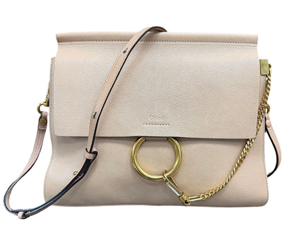 A light beige leather shoulder bag with a flap closure, a large gold-tone O-ring, a gold chain detail, and a thin black-and-beige strap, shown on a plain white background.