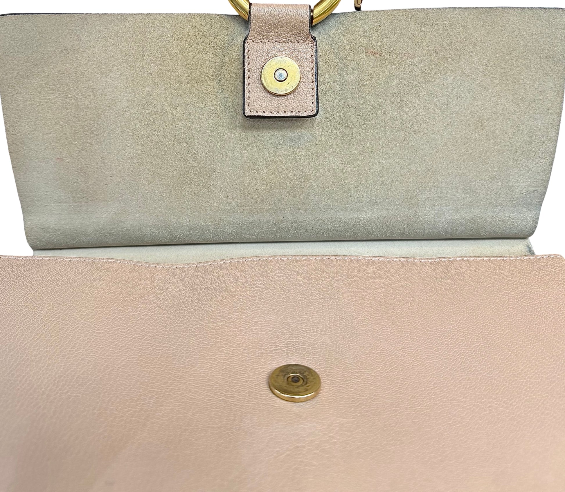 Close-up of a handbag showing the interior flap in beige suede with a gold snap button.