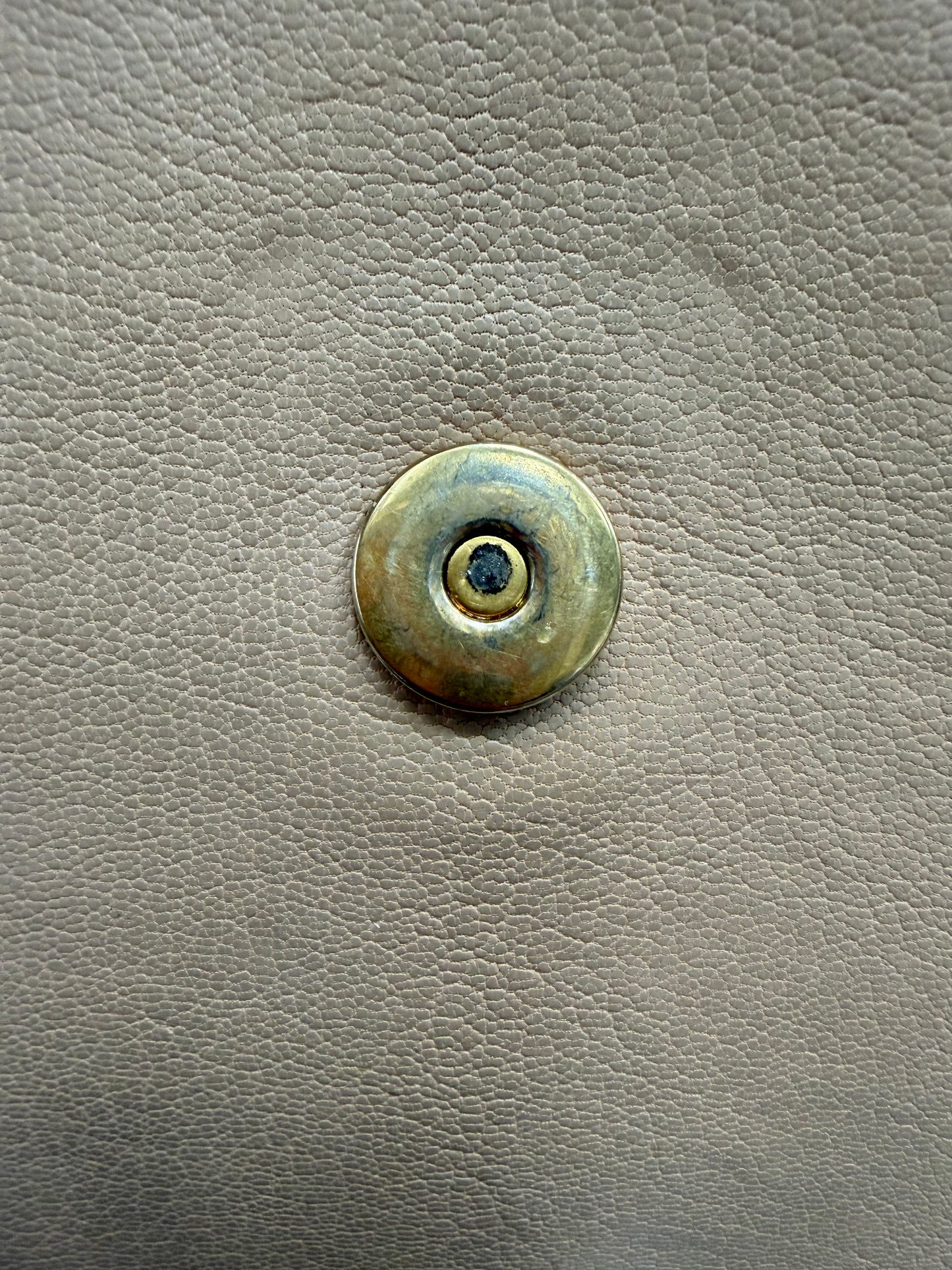 Close up of gold hardware button with scratches and discoloration