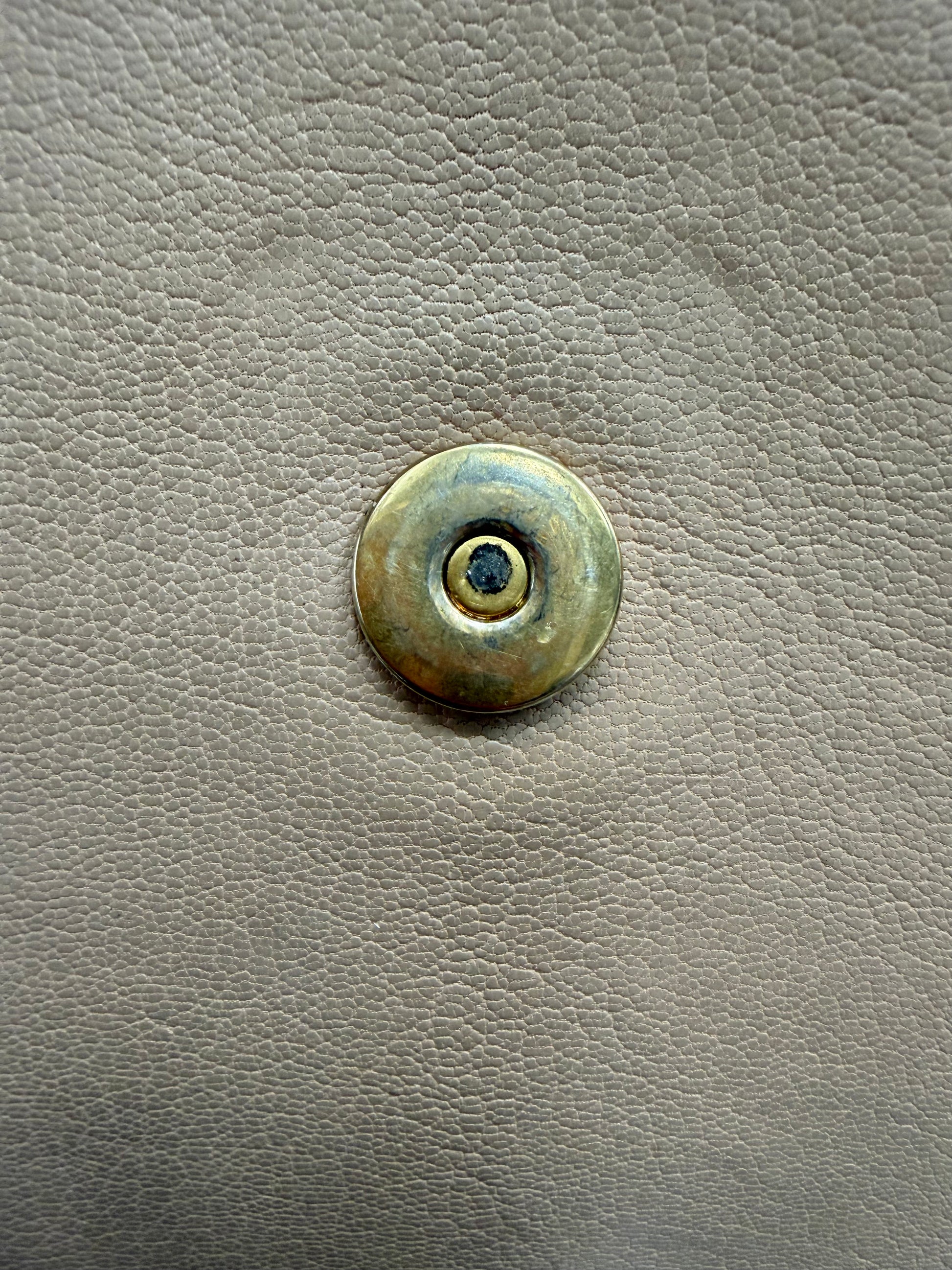 Close up of gold hardware button with scratches and discoloration