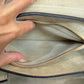 Close-up of a hand opening the interior beige suede zipper pocket with a gold zipper and black trim.