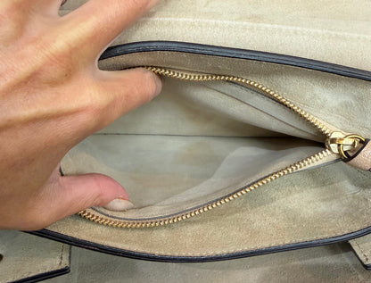 Close-up of a hand opening the interior beige suede zipper pocket with a gold zipper and black trim.