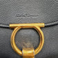 Close-up of a black pebbled leather handbag featuring a large gold-tone metal O-ring clasp and an embossed "Salvatore Ferragamo" logo on the flap.
