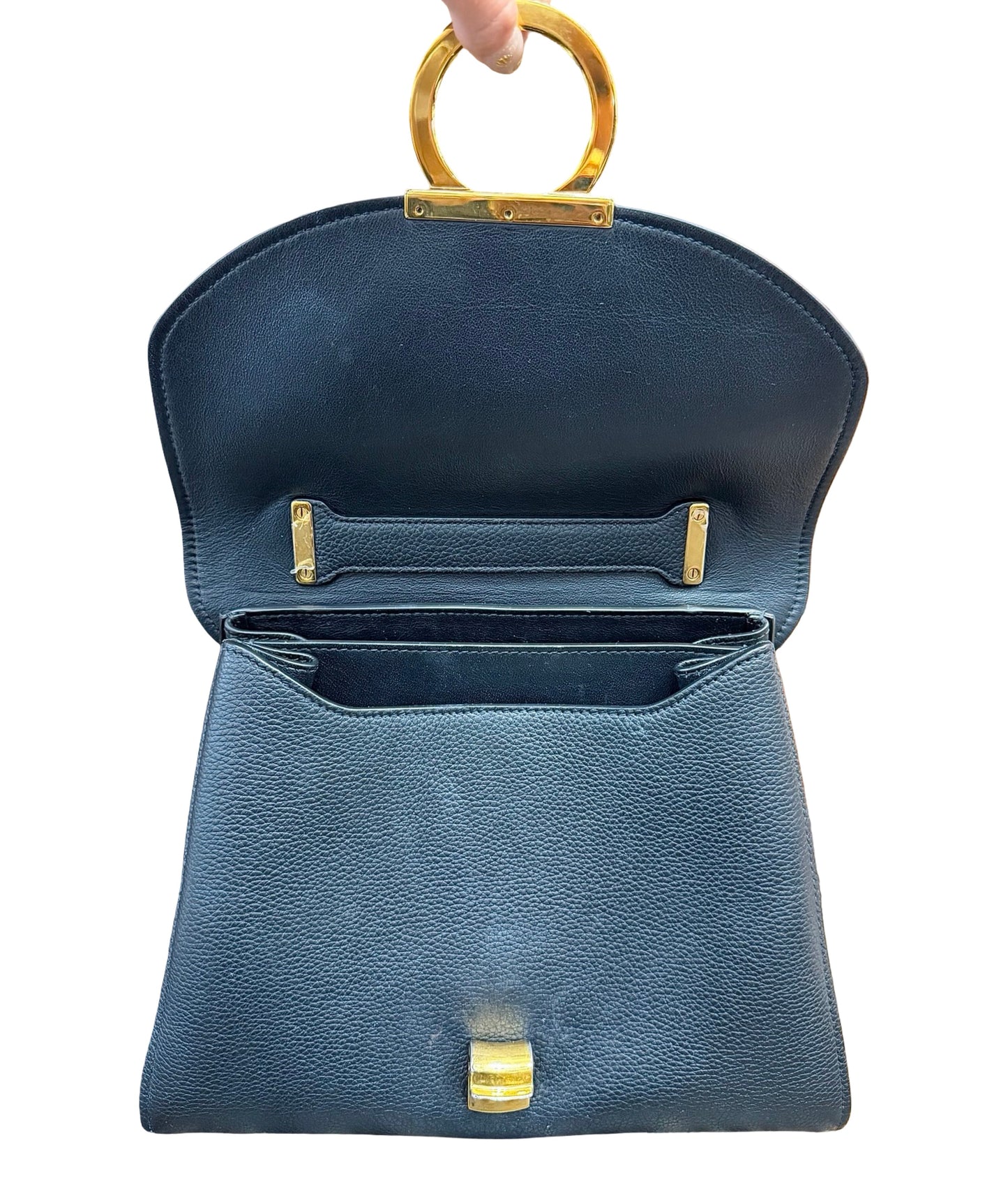 A black pebbled leather handbag with gold-tone hardware, shown open with a circular top handle being held by a hand against a white background.