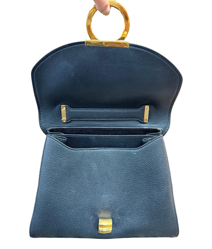 A black pebbled leather handbag with gold-tone hardware, shown open with a circular top handle being held by a hand against a white background.