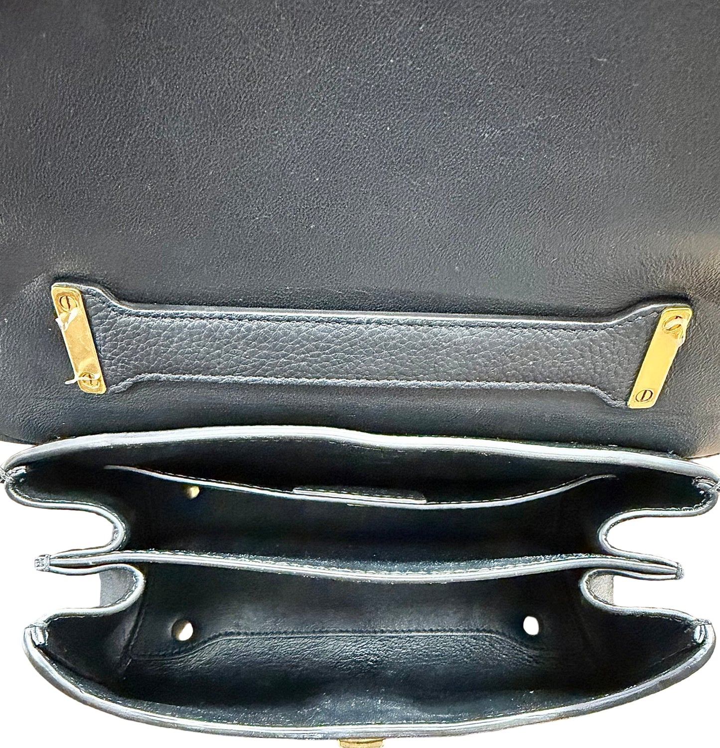 Close-up of the interior of the black handbag, showing multiple interior compartments and gold-tone metal hardware on a white background.
