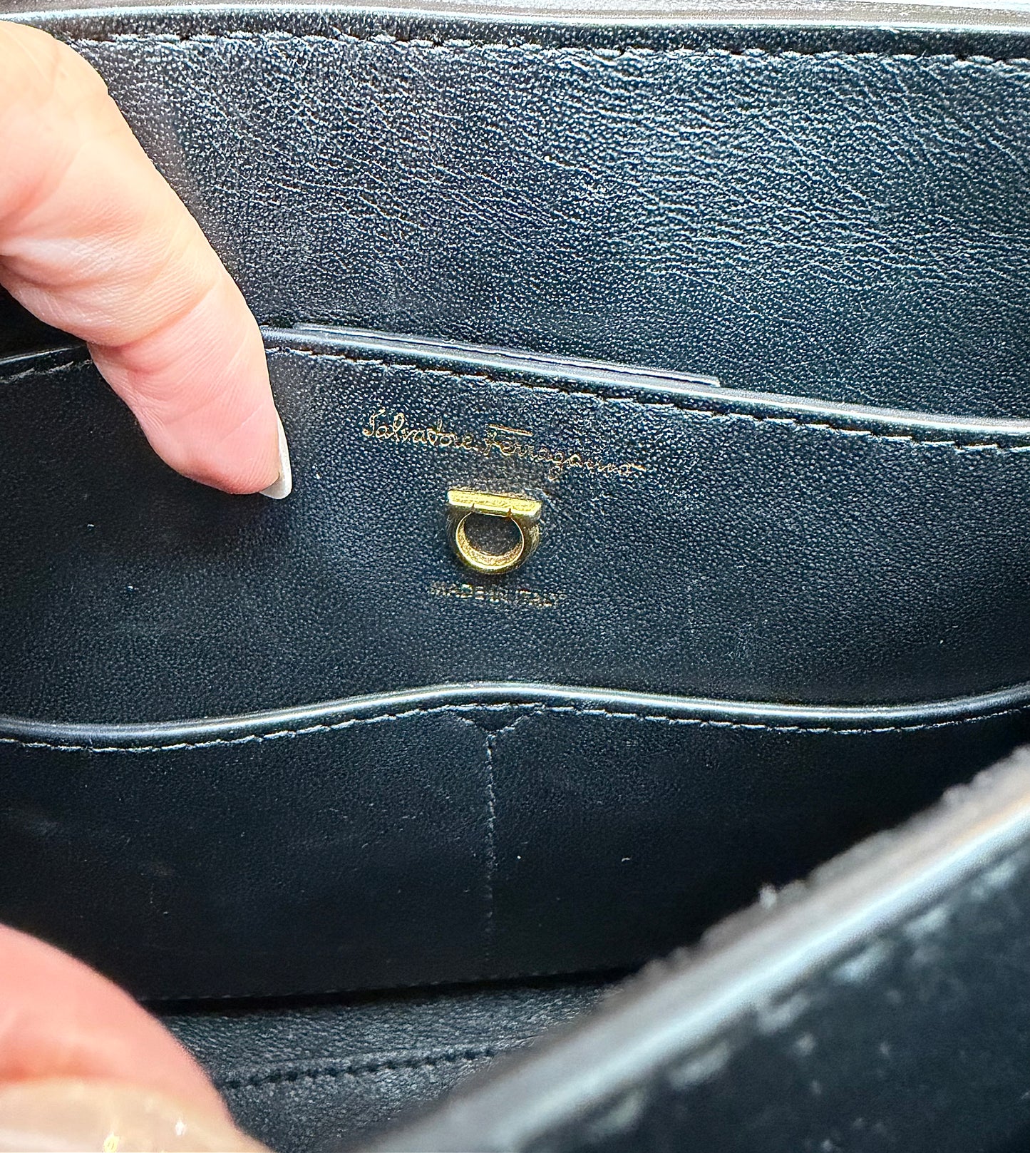 Close-up of the interior of a black leather handbag showing the gold-tone Salvatore Ferragamo signature ring hardware and embossed brand name.