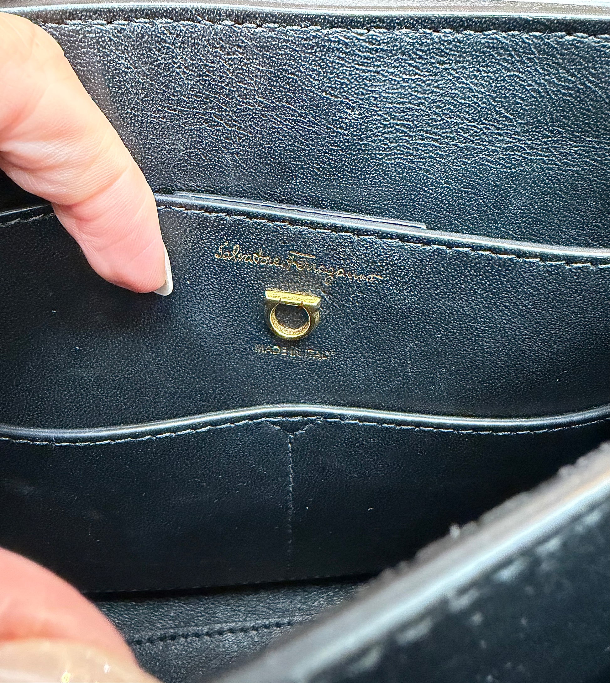 Close-up of the interior of a black leather handbag showing the gold-tone Salvatore Ferragamo signature ring hardware and embossed brand name.