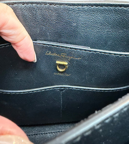 Close-up of the interior of a black leather handbag showing the gold-tone Salvatore Ferragamo signature ring hardware and embossed brand name.