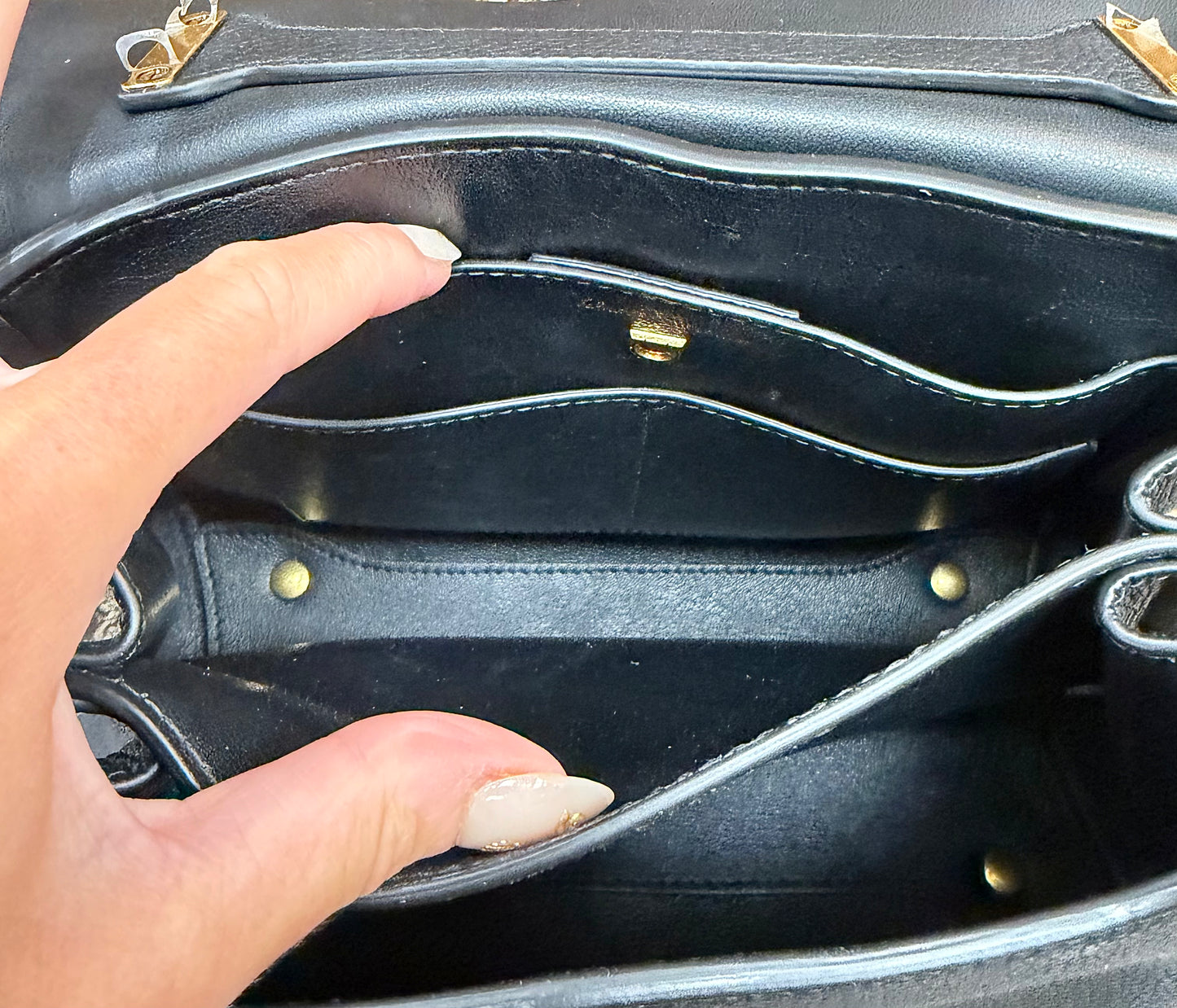 Close-up of the interior of a black leather handbag showing multiple card slots, gold-tone hardware, and a hand keeping the bag open.